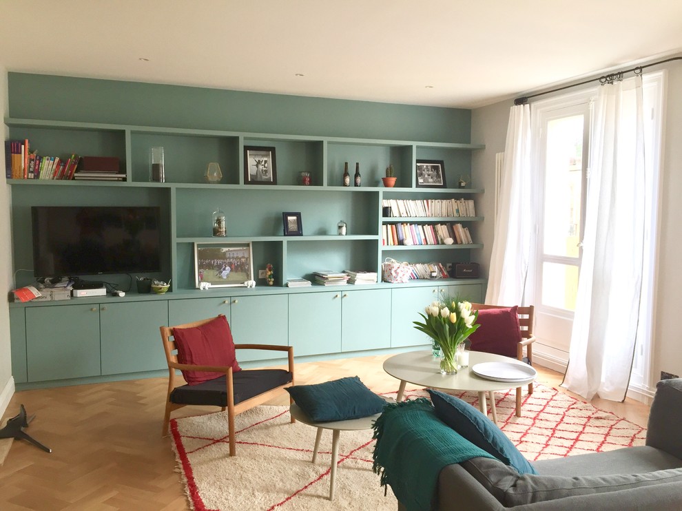 Esempio di un grande soggiorno boho chic aperto con libreria, pareti verdi, parquet chiaro, TV a parete e pavimento beige