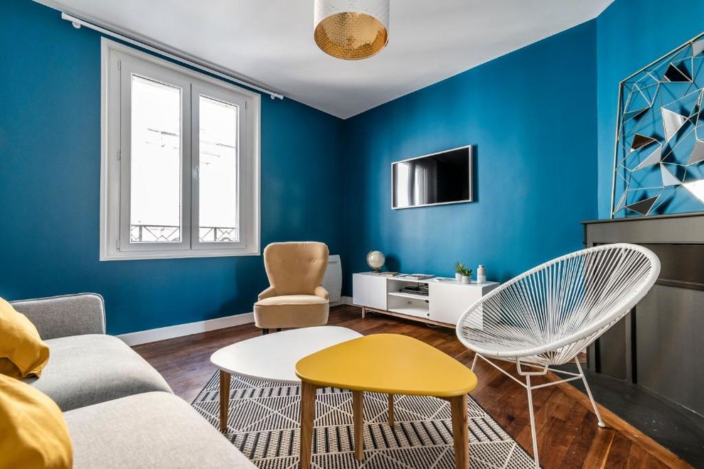 Foto di un soggiorno design di medie dimensioni con pareti blu, pavimento in legno massello medio, camino ad angolo, cornice del camino in intonaco, TV a parete e pavimento marrone
