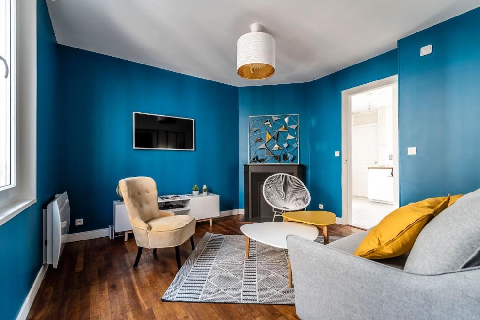 Modelo de salón actual de tamaño medio con paredes azules, suelo de madera en tonos medios, chimenea de esquina, marco de chimenea de yeso, televisor colgado en la pared y suelo marrón