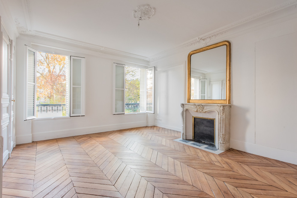 Cette image montre un grand salon traditionnel avec un mur blanc, un sol en bois brun, une cheminée standard et un sol beige.