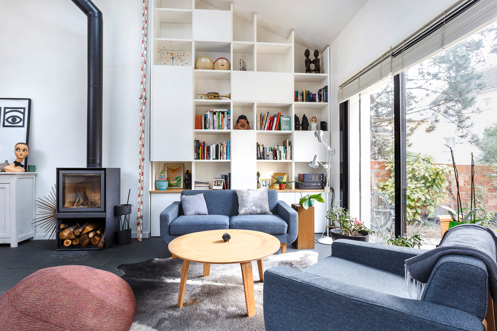 Immagine di un soggiorno nordico aperto con libreria, pareti bianche, stufa a legna e pavimento nero