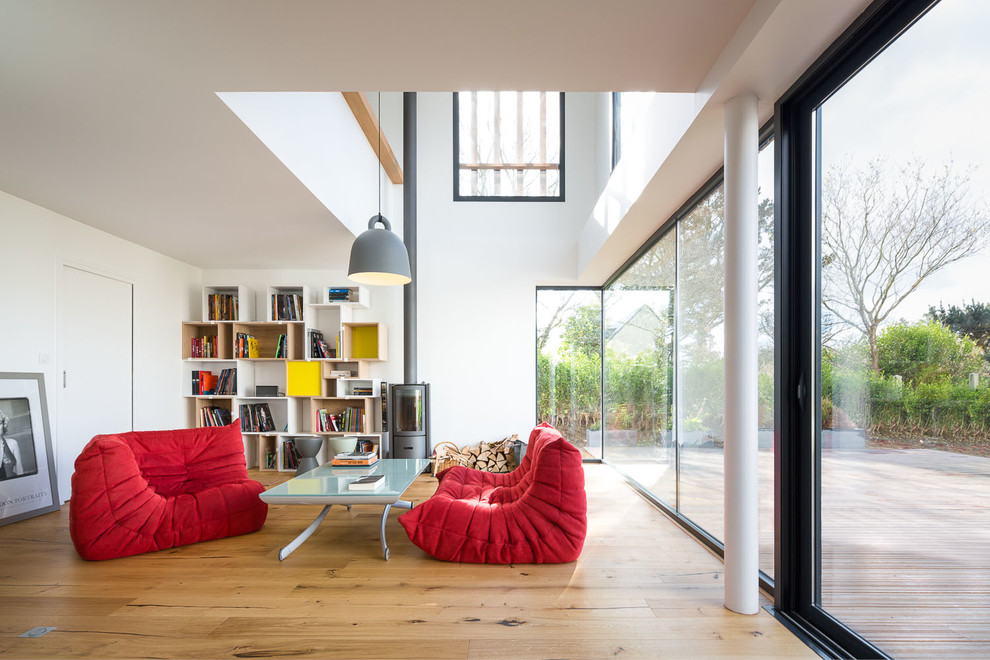 Immagine di un grande soggiorno minimalista aperto con libreria, pareti bianche, parquet chiaro, stufa a legna e nessuna TV