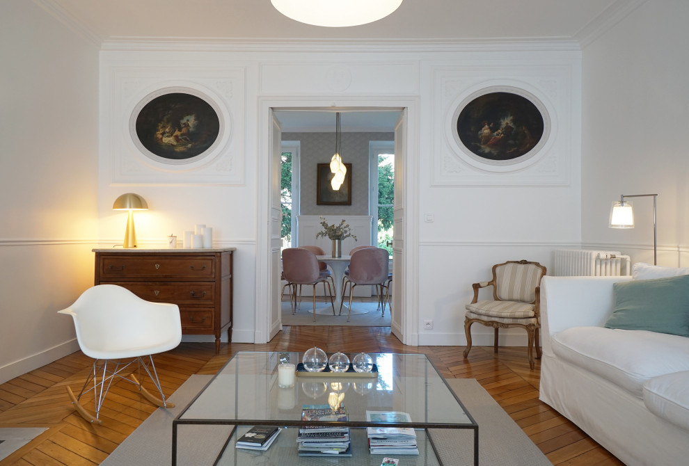 パリにある高級な中くらいなトランジショナルスタイルのおしゃれなLDK (白い壁、淡色無垢フローリング、標準型暖炉、石材の暖炉まわり、テレビなし、茶色い床) の写真