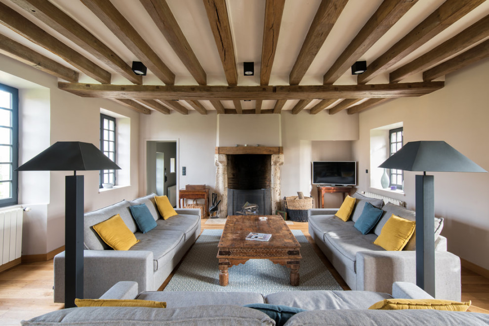 Immagine di un soggiorno country aperto con pareti beige, pavimento in legno massello medio, camino classico, pavimento marrone e travi a vista