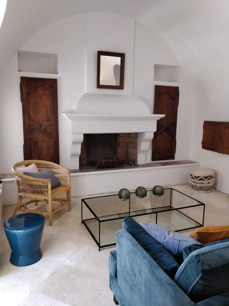Diseño de salón abierto y abovedado mediterráneo de tamaño medio sin televisor con paredes blancas, suelo de travertino, todas las chimeneas, marco de chimenea de yeso y suelo beige