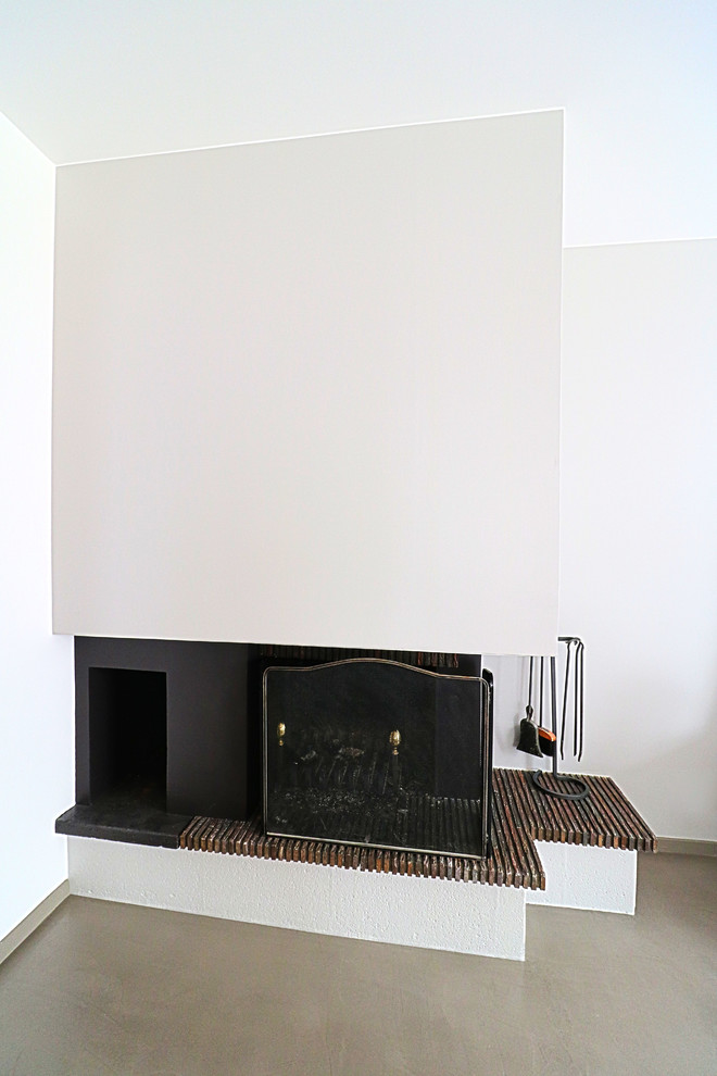Réalisation d'un salon design de taille moyenne avec sol en béton ciré, une cheminée d'angle, un manteau de cheminée en plâtre et un sol gris.