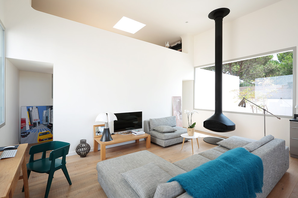 This is an example of a medium sized contemporary open plan living room in Paris with white walls, light hardwood flooring, a freestanding tv, a wood burning stove and feature lighting.