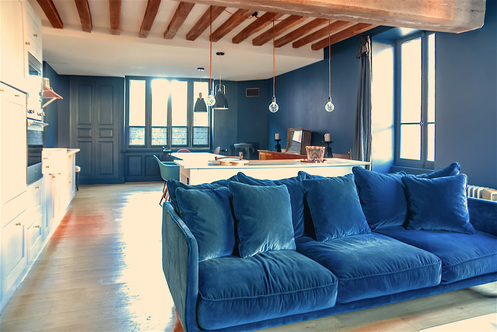 Modelo de salón abierto campestre extra grande sin chimenea y televisor con paredes azules y suelo de madera clara