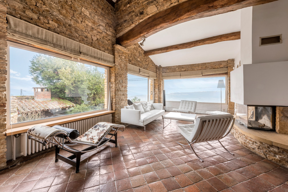 Cette photo montre un grand salon méditerranéen avec un mur beige, tomettes au sol, aucun téléviseur, une salle de réception et une cheminée double-face.