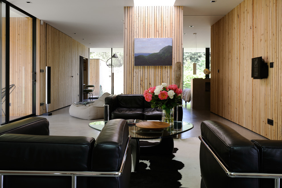 Modelo de salón para visitas abierto contemporáneo de tamaño medio sin chimenea con paredes marrones, suelo de cemento y televisor colgado en la pared