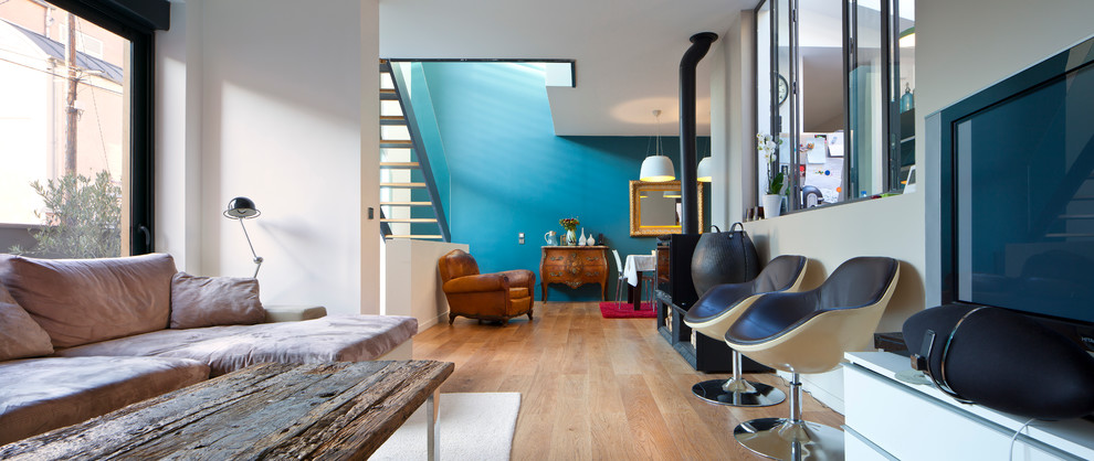 Foto de salón abierto contemporáneo de tamaño medio con paredes azules, suelo de madera clara, estufa de leña, marco de chimenea de metal y televisor independiente