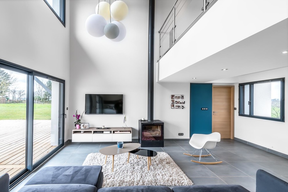 Photo of a contemporary open plan living room in Clermont-Ferrand with white walls, concrete flooring, a wood burning stove, a metal fireplace surround, a wall mounted tv and grey floors.