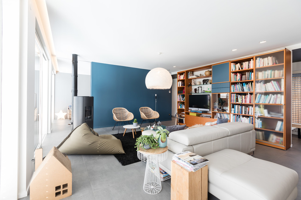 Foto de biblioteca en casa abierta contemporánea grande con paredes azules, suelo de baldosas de cerámica, estufa de leña, marco de chimenea de metal, televisor independiente y suelo gris