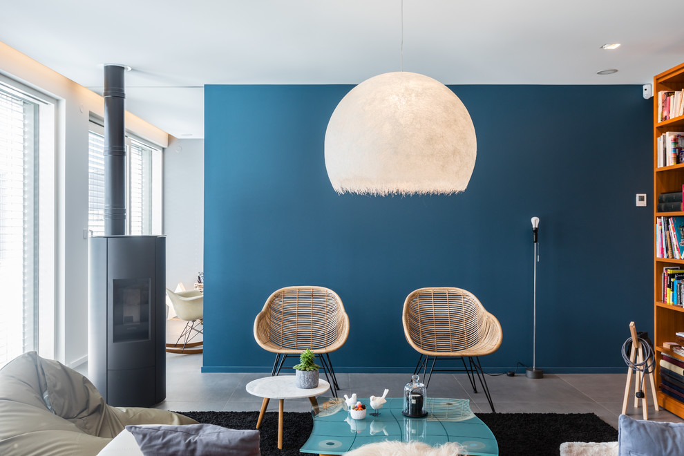 Идея дизайна: открытая гостиная комната среднего размера в современном стиле с с книжными шкафами и полками, синими стенами, полом из керамической плитки, печью-буржуйкой, фасадом камина из металла, отдельно стоящим телевизором и серым полом