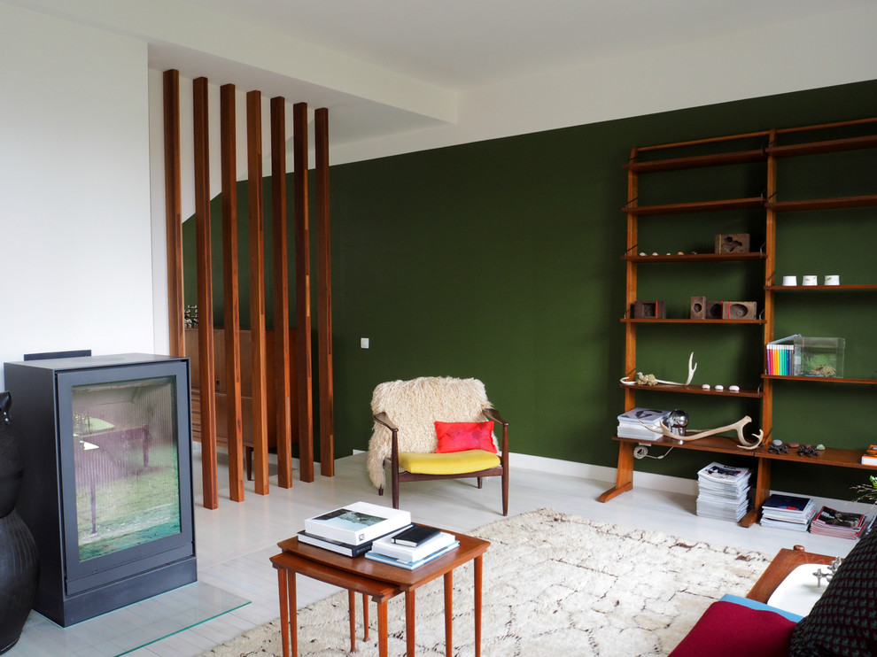 На фото: большая открытая гостиная комната в современном стиле с с книжными шкафами и полками, зелеными стенами, деревянным полом и печью-буржуйкой без телевизора