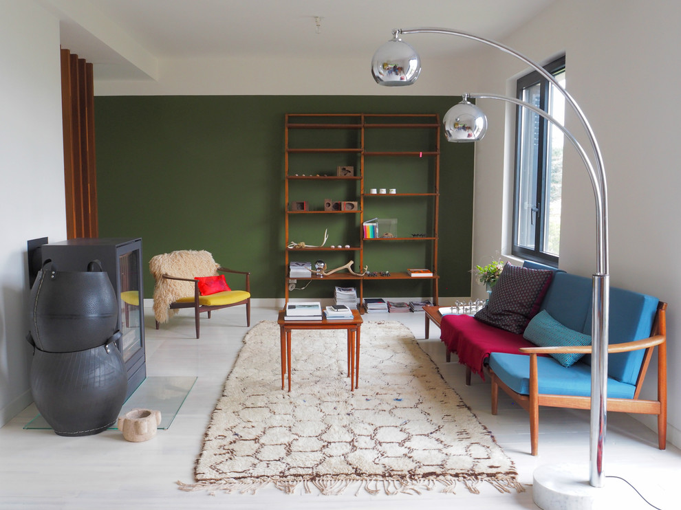 Пример оригинального дизайна: большая открытая гостиная комната в современном стиле с с книжными шкафами и полками, зелеными стенами, деревянным полом и печью-буржуйкой без телевизора