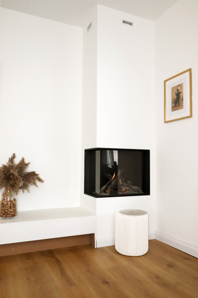 Modelo de salón abierto moderno grande con paredes blancas, suelo de madera en tonos medios, estufa de leña, marco de chimenea de yeso, televisor independiente y suelo beige