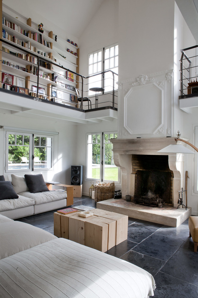 Стильный дизайн: открытая гостиная комната в белых тонах с отделкой деревом в стиле фьюжн с белыми стенами, стандартным камином, фасадом камина из камня и черным полом - последний тренд