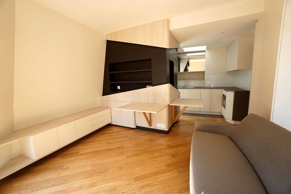 Modelo de biblioteca en casa tipo loft actual pequeña con paredes blancas, suelo de madera clara, televisor colgado en la pared y suelo marrón