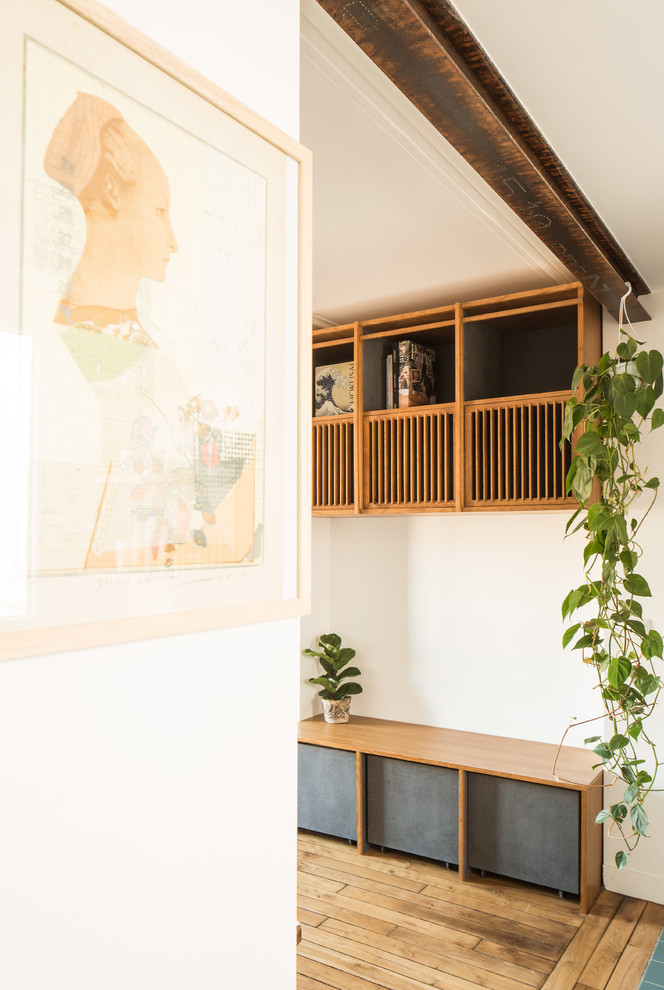 Foto på ett mellanstort skandinaviskt allrum med öppen planlösning, med ett bibliotek, vita väggar, ljust trägolv, en spiselkrans i trä och en dold TV