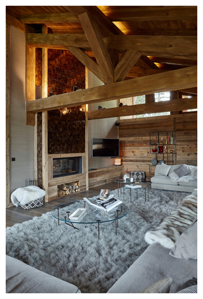 Large rustic open plan living room in Lyon with grey walls, medium hardwood flooring, a two-sided fireplace, a wooden fireplace surround and a wall mounted tv.