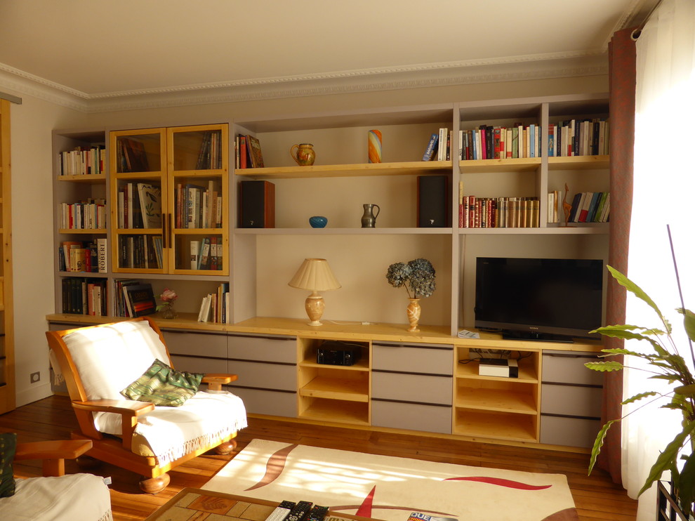Cette image montre un salon bohème de taille moyenne et ouvert avec une bibliothèque ou un coin lecture, un mur jaune, parquet foncé, un téléviseur encastré et un sol marron.