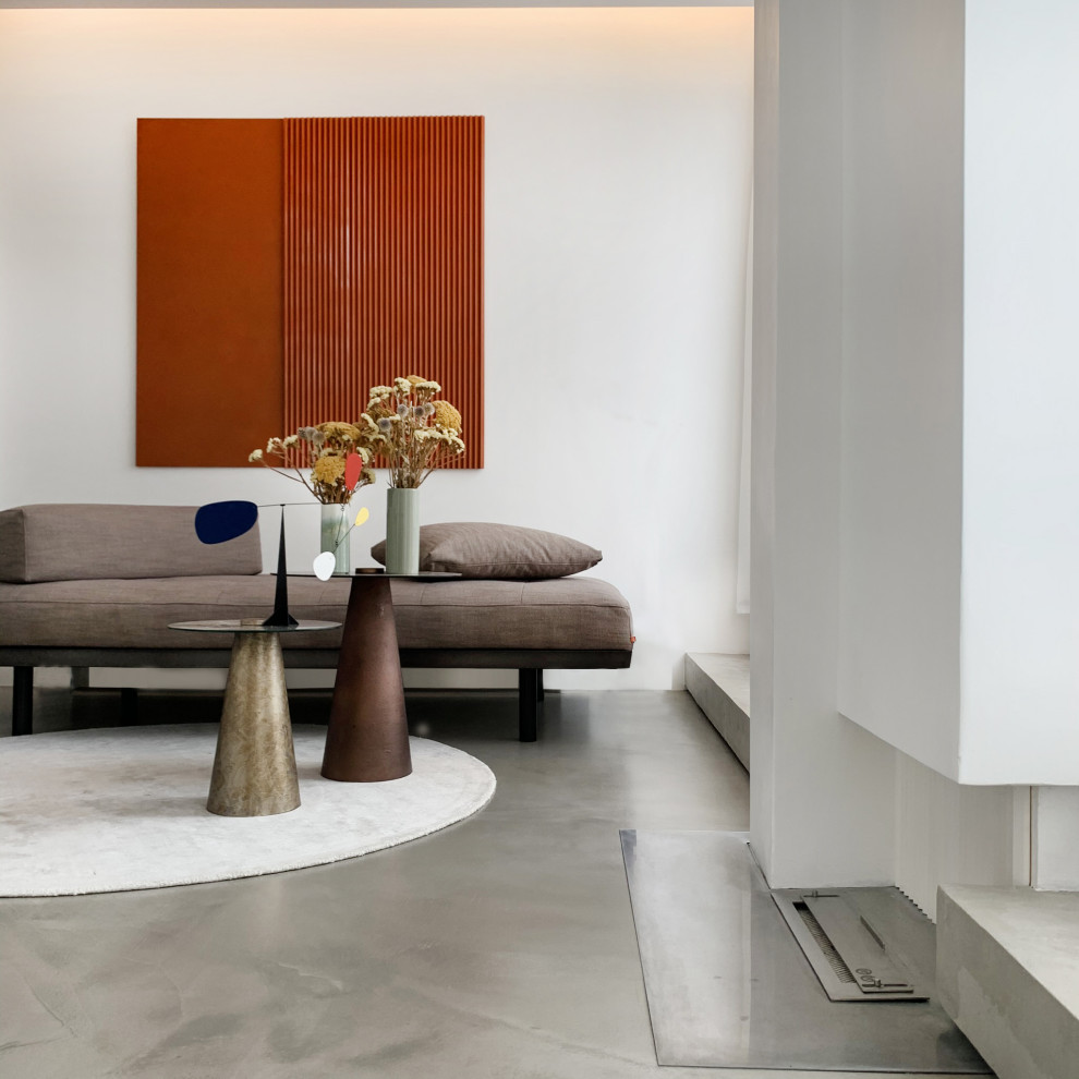 Cette image montre un salon design avec sol en béton ciré, cheminée suspendue, un manteau de cheminée en plâtre et un sol gris.