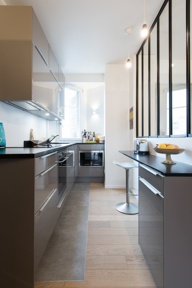 This is an example of a contemporary l-shaped enclosed kitchen in Paris with a submerged sink, flat-panel cabinets, grey cabinets, no island, grey floors and black worktops.