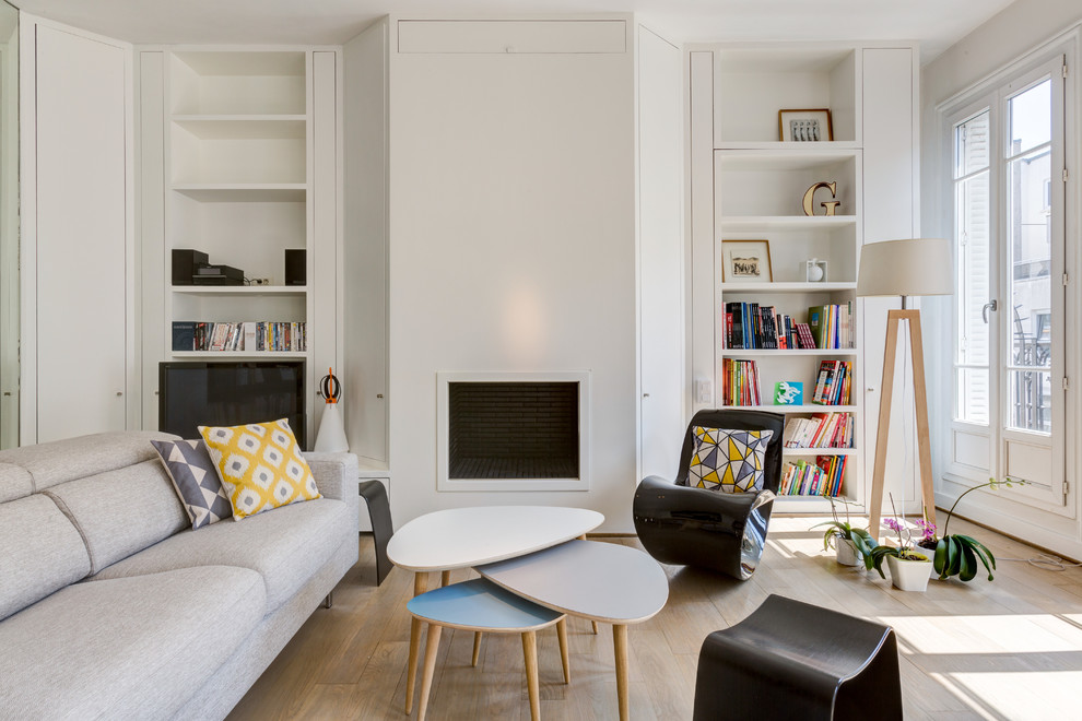 Cette image montre un grand salon nordique ouvert avec une bibliothèque ou un coin lecture, un mur blanc, parquet clair, aucune cheminée, un téléviseur indépendant et un sol beige.
