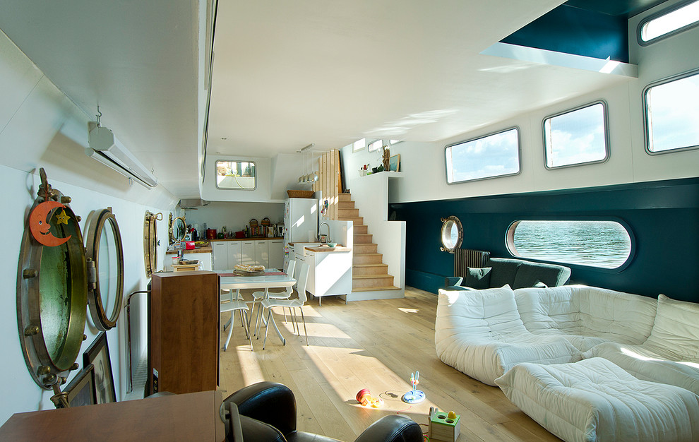 Modern inredning av ett stort allrum med öppen planlösning, med blå väggar, ljust trägolv, en öppen vedspis och beiget golv