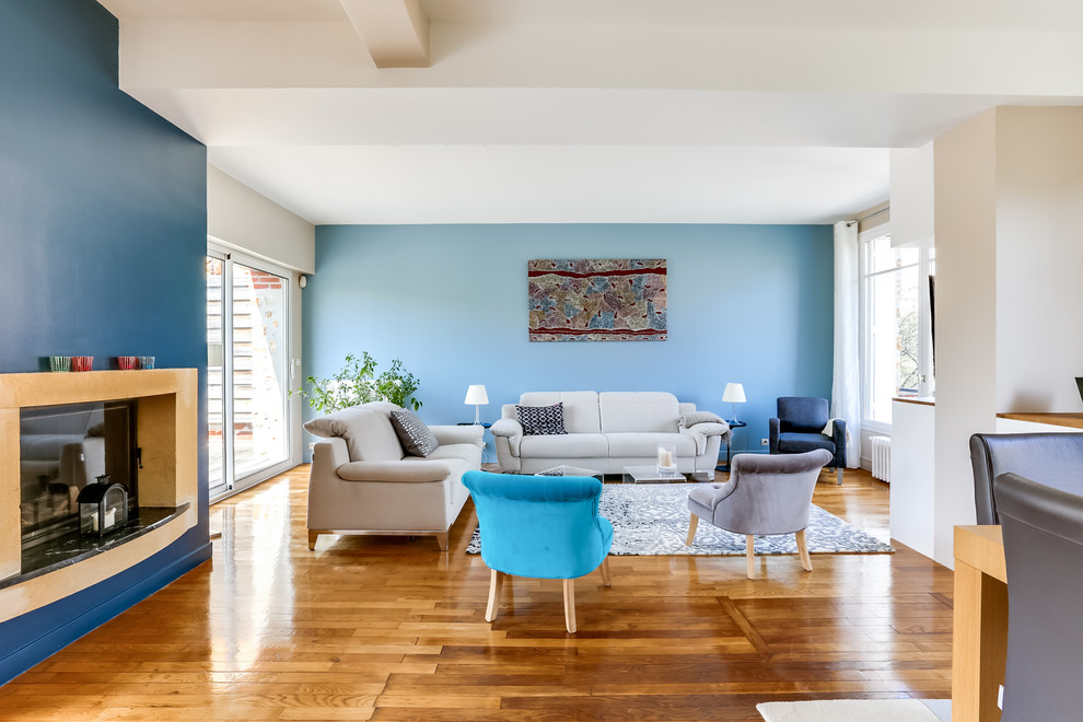 Idées déco pour un grand salon contemporain avec un mur bleu, parquet clair, une cheminée standard, un manteau de cheminée en plâtre et un téléviseur fixé au mur.