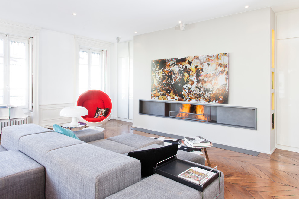 Mittelgroßes, Offenes, Repräsentatives, Fernseherloses Modernes Wohnzimmer mit weißer Wandfarbe, braunem Holzboden, Gaskamin und Kaminumrandung aus Beton in Lyon