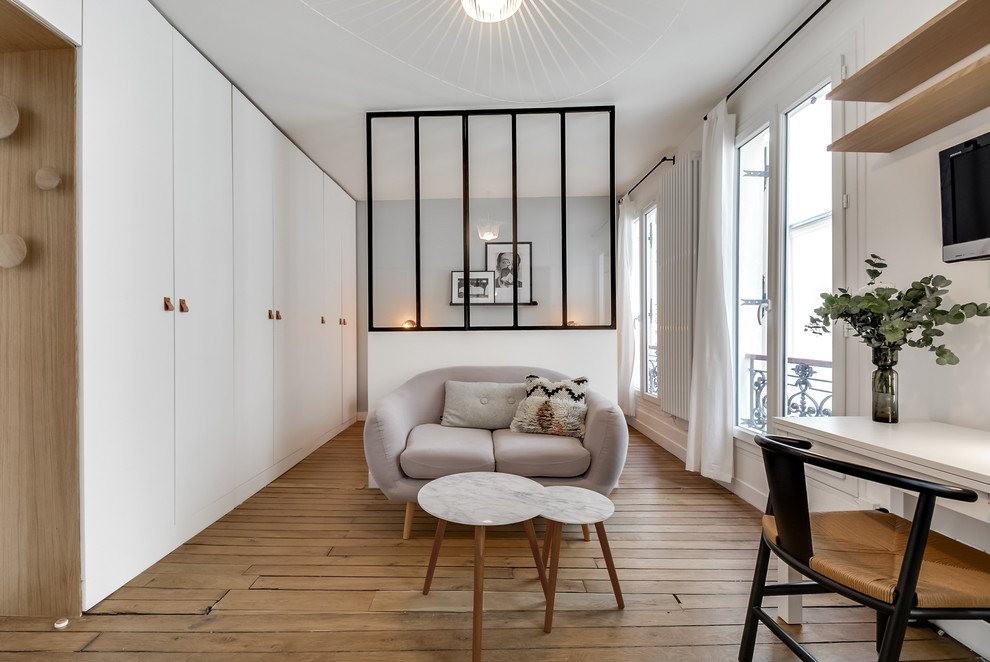 This is an example of a medium sized contemporary open plan living room in Paris with white walls, light hardwood flooring and a wall mounted tv.