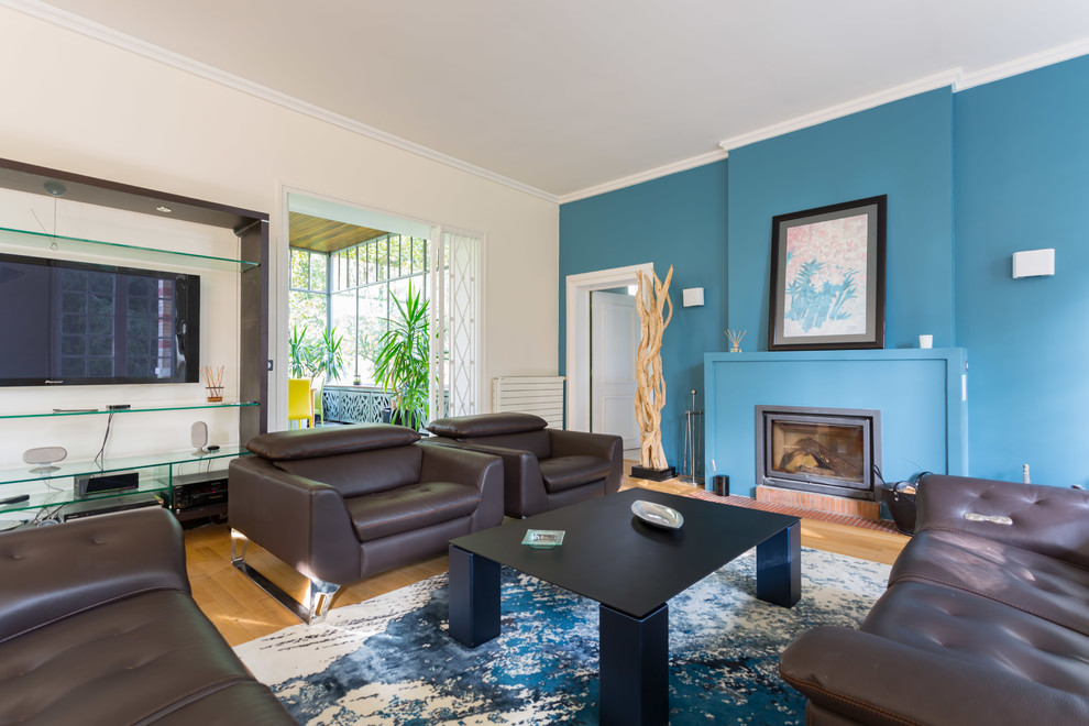 Immagine di un grande soggiorno minimalista aperto con pareti blu, parquet chiaro, camino classico, cornice del camino in intonaco, TV a parete e pavimento beige