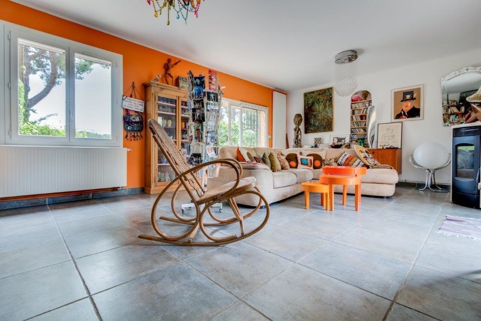 Idee per un grande soggiorno bohémian aperto con pareti arancioni, pavimento grigio, libreria, pavimento con piastrelle in ceramica, stufa a legna, cornice del camino in metallo e nessuna TV