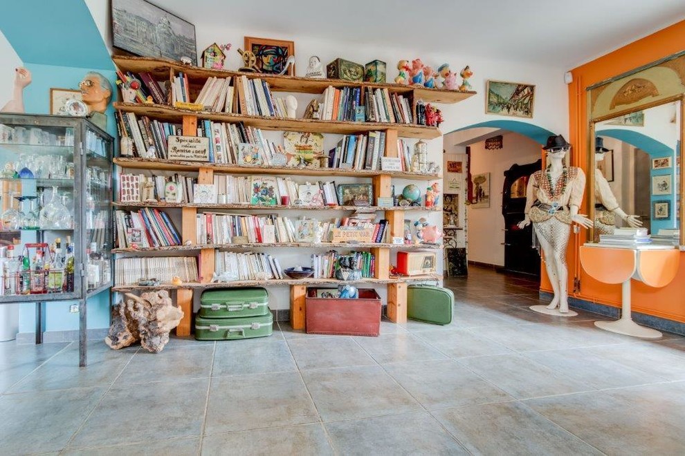 Bild på ett stort eklektiskt allrum med öppen planlösning, med ett bibliotek, orange väggar, klinkergolv i keramik, en öppen vedspis, en spiselkrans i metall och grått golv