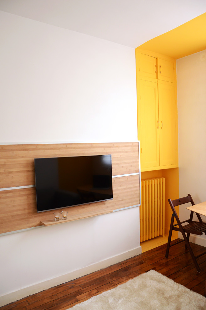 Cette image montre un petit salon design fermé avec un mur jaune, parquet foncé, aucune cheminée et un téléviseur fixé au mur.