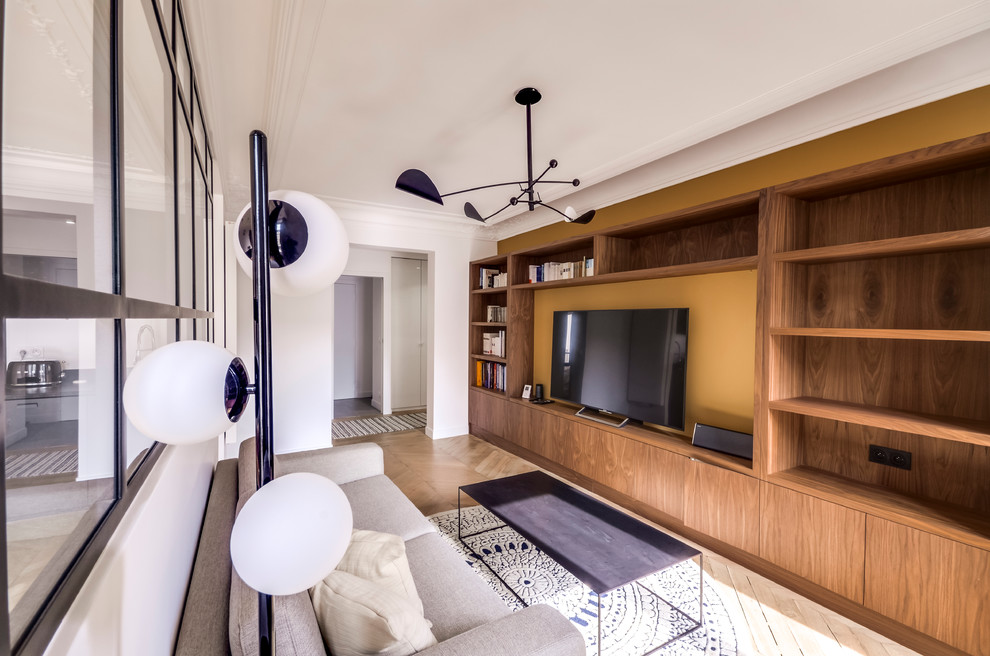 Modelo de biblioteca en casa abierta retro de tamaño medio con paredes amarillas, suelo de madera clara y televisor independiente