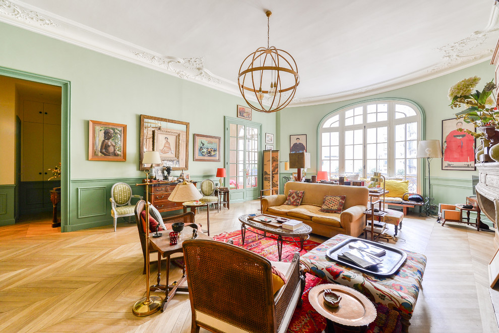 Klassisches Wohnzimmer mit grüner Wandfarbe, hellem Holzboden, Kamin, Kaminumrandung aus Stein und braunem Boden in Paris