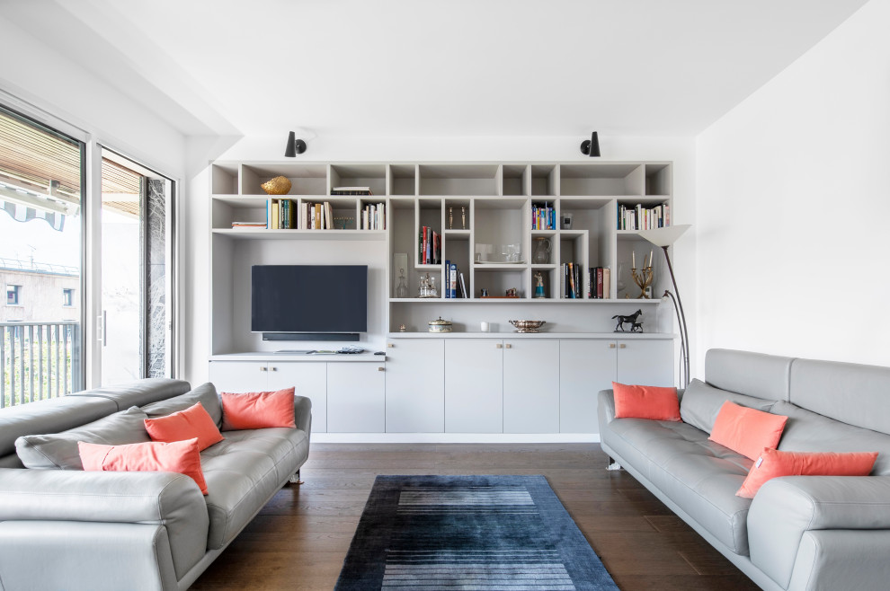 Cette image montre un salon design avec un mur blanc, parquet foncé, un téléviseur encastré et un sol marron.