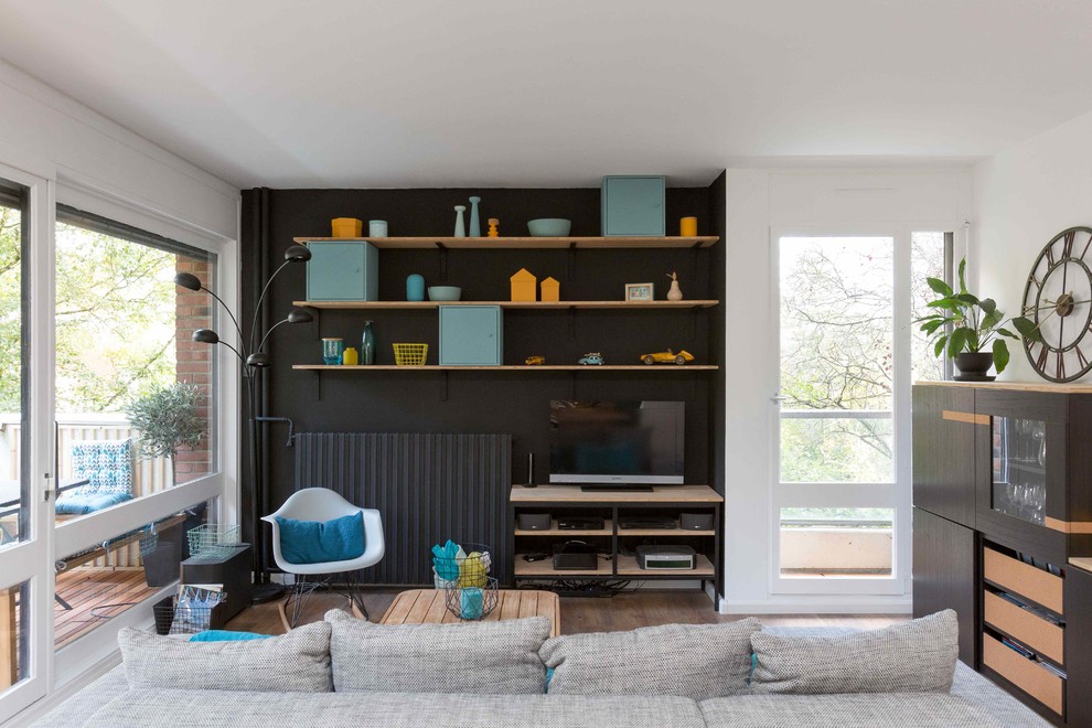 Foto di un grande soggiorno minimal aperto con pareti nere, pavimento in legno massello medio e TV nascosta