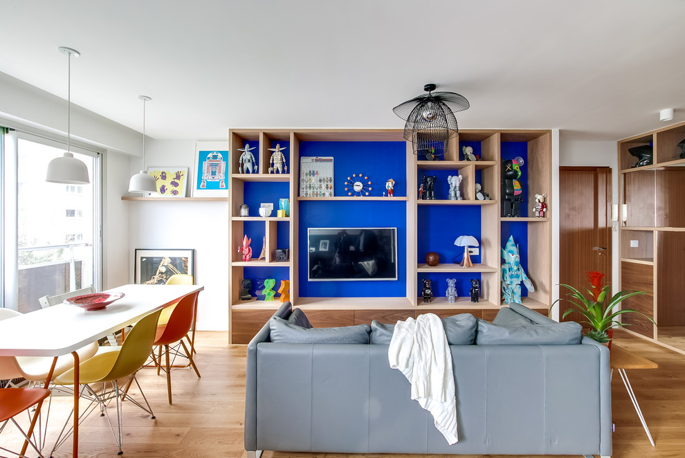 Inredning av ett modernt mellanstort allrum med öppen planlösning, med ett bibliotek, blå väggar, ljust trägolv och en väggmonterad TV