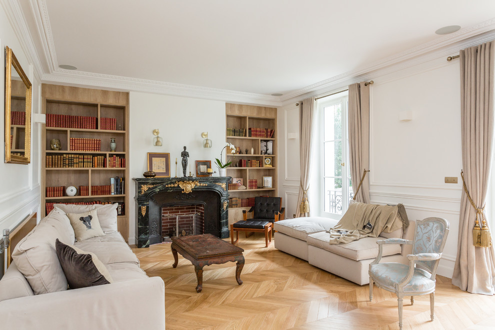 Cette photo montre un grand salon chic ouvert avec une bibliothèque ou un coin lecture, un mur blanc, un sol en bois brun, une cheminée standard, un sol marron et un manteau de cheminée en pierre.