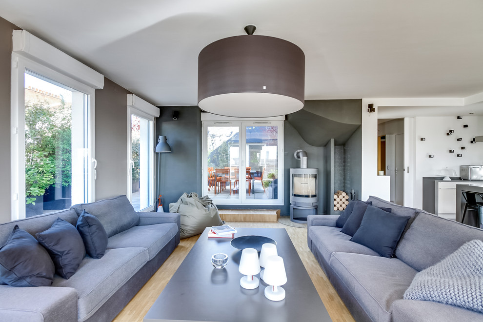 Großes, Offenes Modernes Wohnzimmer mit grauer Wandfarbe, hellem Holzboden, Kaminofen, freistehendem TV, braunem Boden und Kaminumrandung aus Metall in Paris