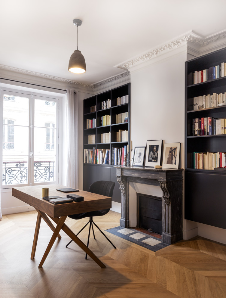 Cette photo montre un grand bureau tendance avec une bibliothèque ou un coin lecture, un mur blanc, parquet clair, une cheminée standard, un manteau de cheminée en pierre et un sol marron.