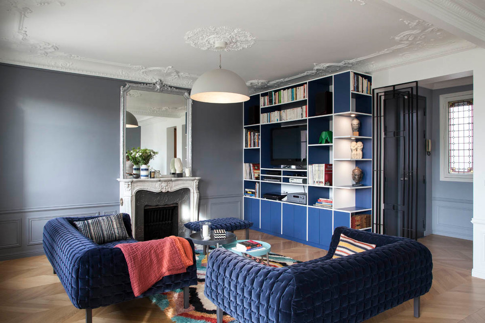 Пример оригинального дизайна: большая гостиная комната в стиле неоклассика (современная классика) с серыми стенами, паркетным полом среднего тона, стандартным камином, телевизором на стене и коричневым полом