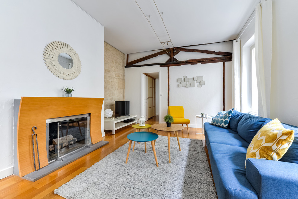 Country Wohnzimmer mit weißer Wandfarbe, hellem Holzboden, Kamin, Kaminumrandung aus Holz, freistehendem TV und braunem Boden in Paris