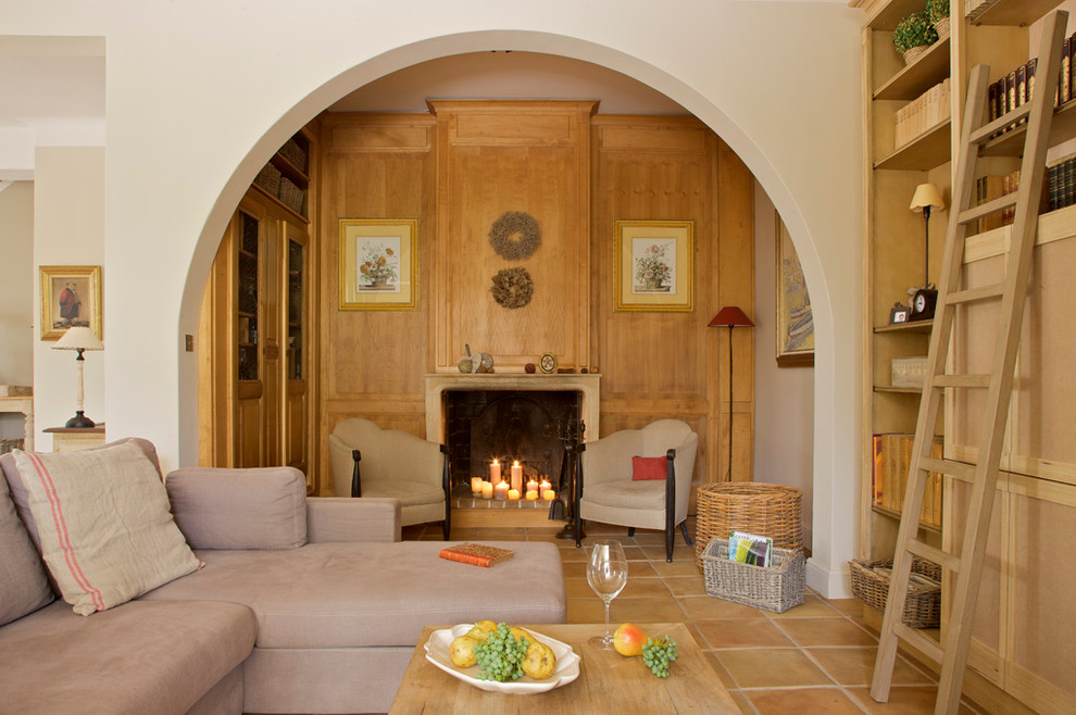 Immagine di un grande soggiorno classico aperto con libreria, pareti beige, pavimento in terracotta, camino classico e nessuna TV