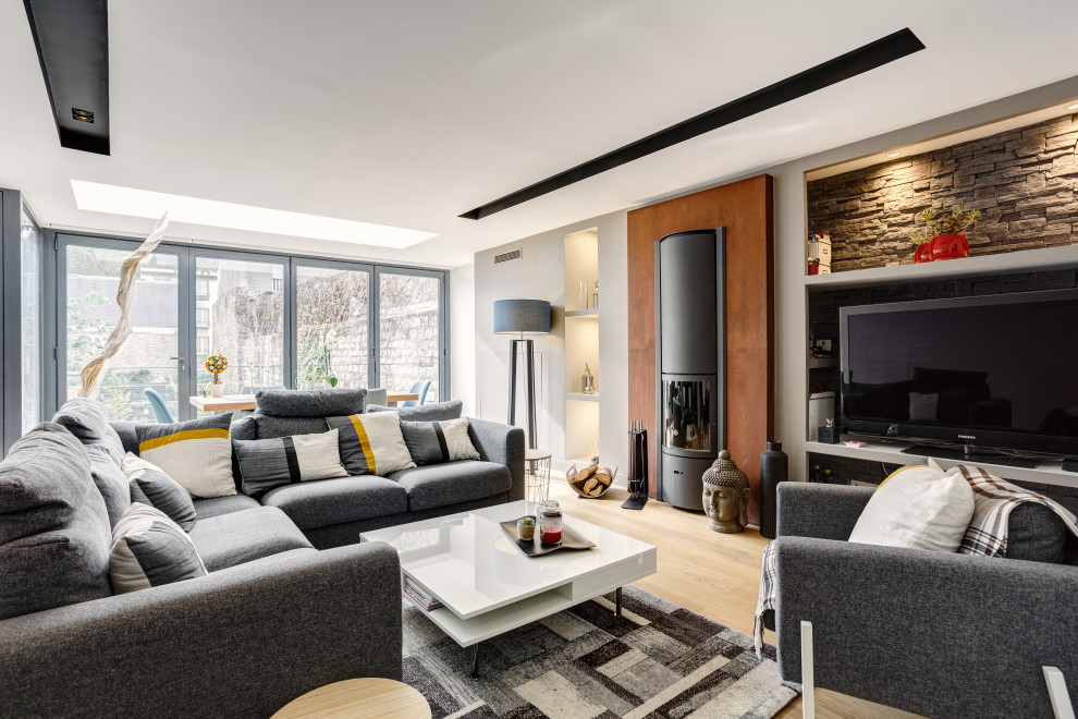 Diseño de salón abierto actual grande con paredes beige, suelo de madera clara, estufa de leña, marco de chimenea de metal, televisor independiente y suelo marrón