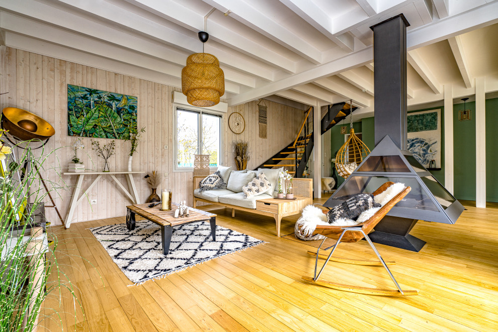 Offenes Wohnzimmer mit beiger Wandfarbe, braunem Holzboden, Kaminofen, braunem Boden, freigelegten Dachbalken und Holzwänden in Angers